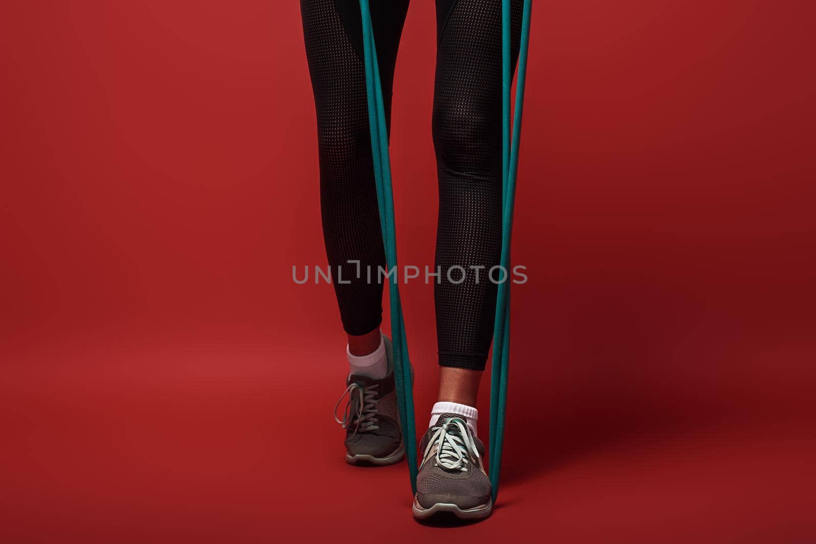 Close up of female legs in sportswear with expander exercising over red background