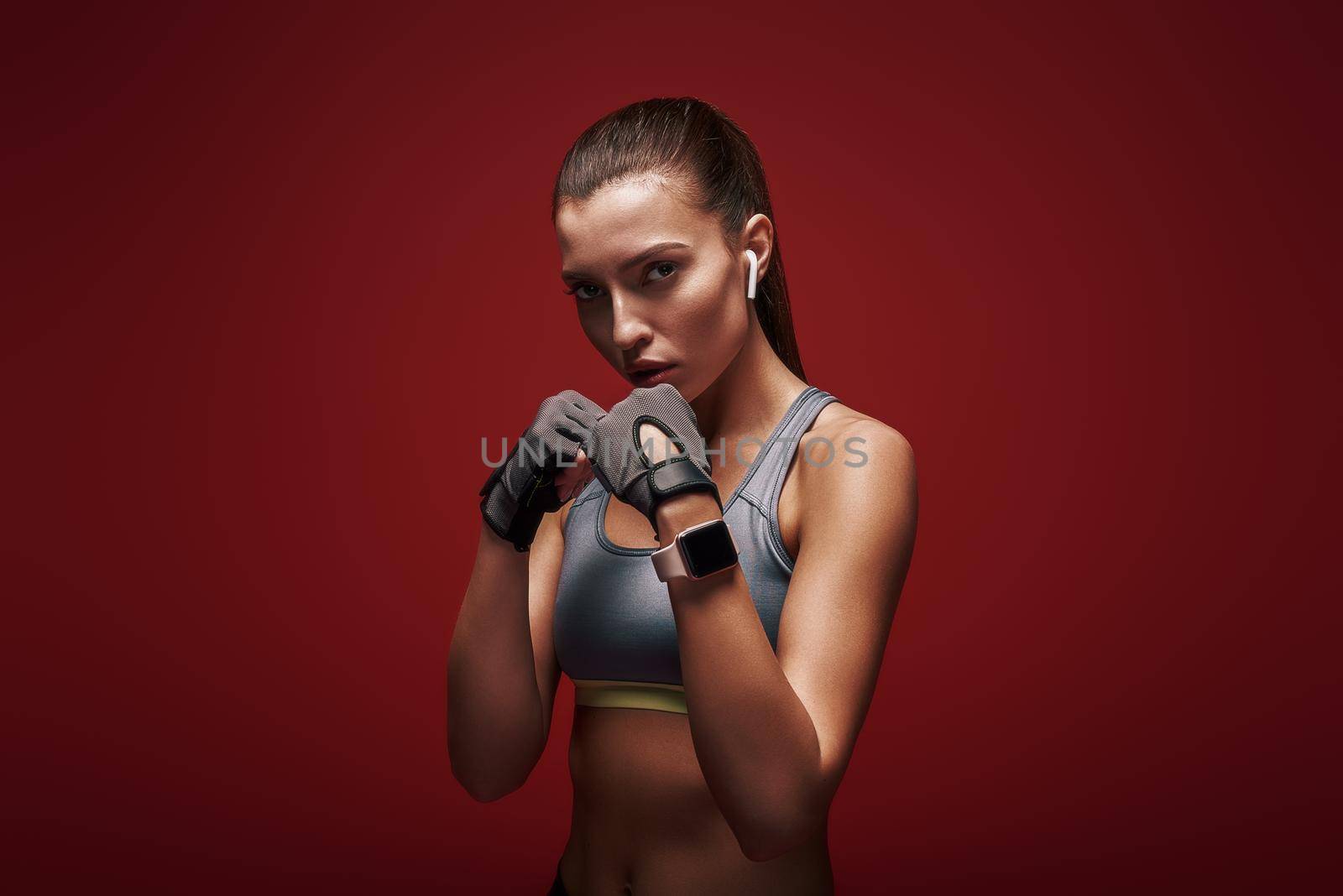 Portrait of young beautiful sportswoman wearing workout gloves. She is ready to fight. Isolated over red background