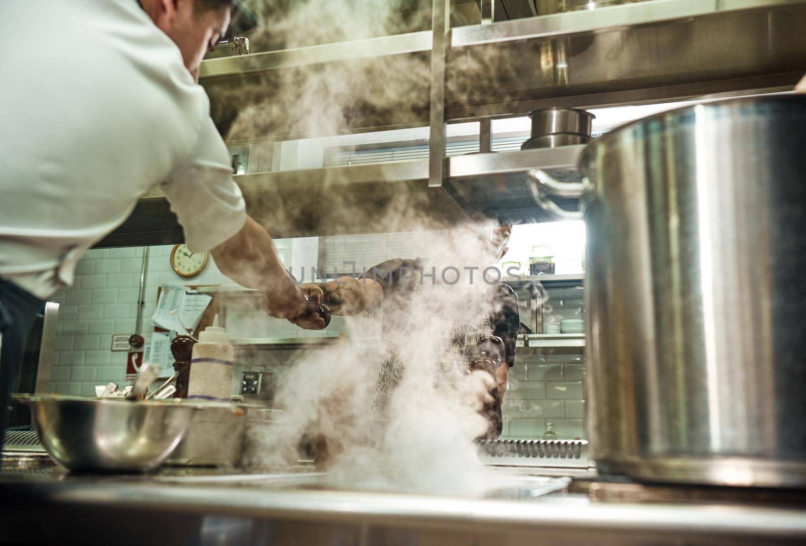 Teamwork. Restaurant chef giving a pepper grinder to his assistant while cooking process at kitchen. Culinary school