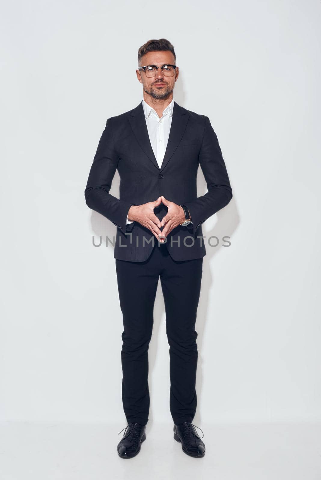 Confidence and success. Full length of handsome businessman in classic wear and eyeglasses looking at camera standing against grey background by friendsstock