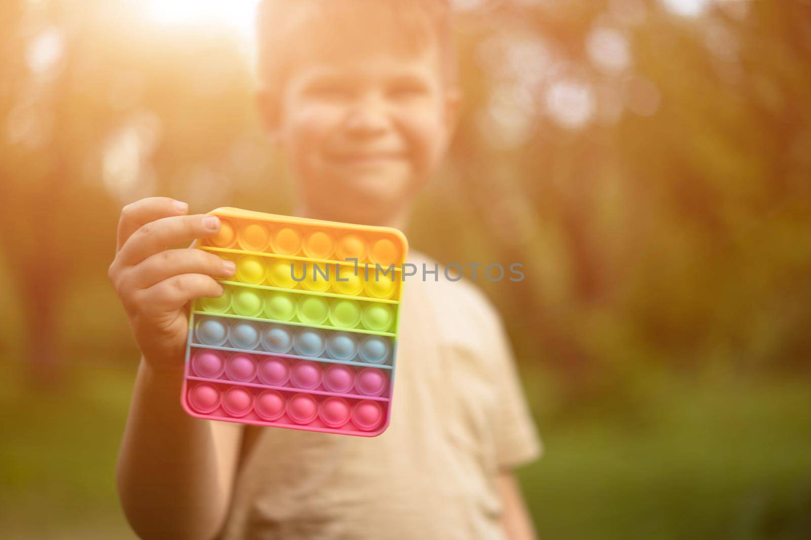 Rainbow Pop It. Toddler Boy Shows his Favorite Sensory Toy. Selective Focus of Colorful Pop It in Sunny Park. High quality photo