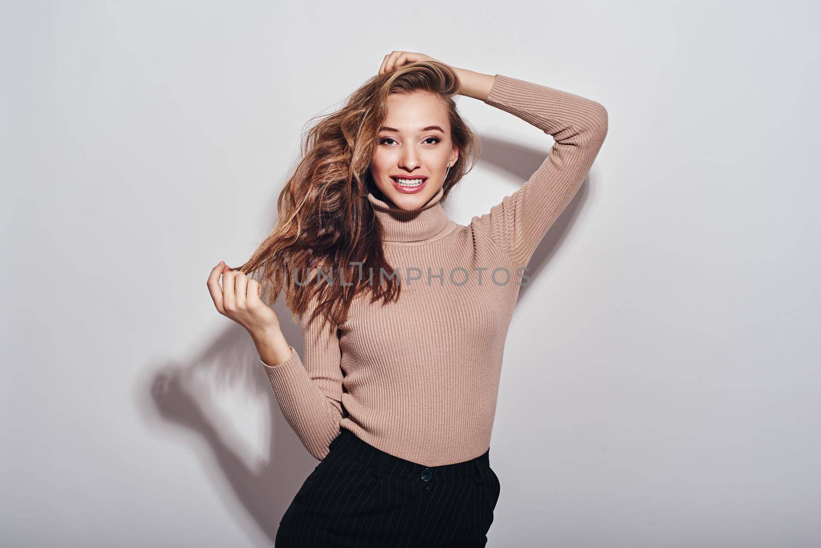 Portrait of young beautiful girl with brown hair, wearing beige turtleneck smiling, looking at camera isolated over white background