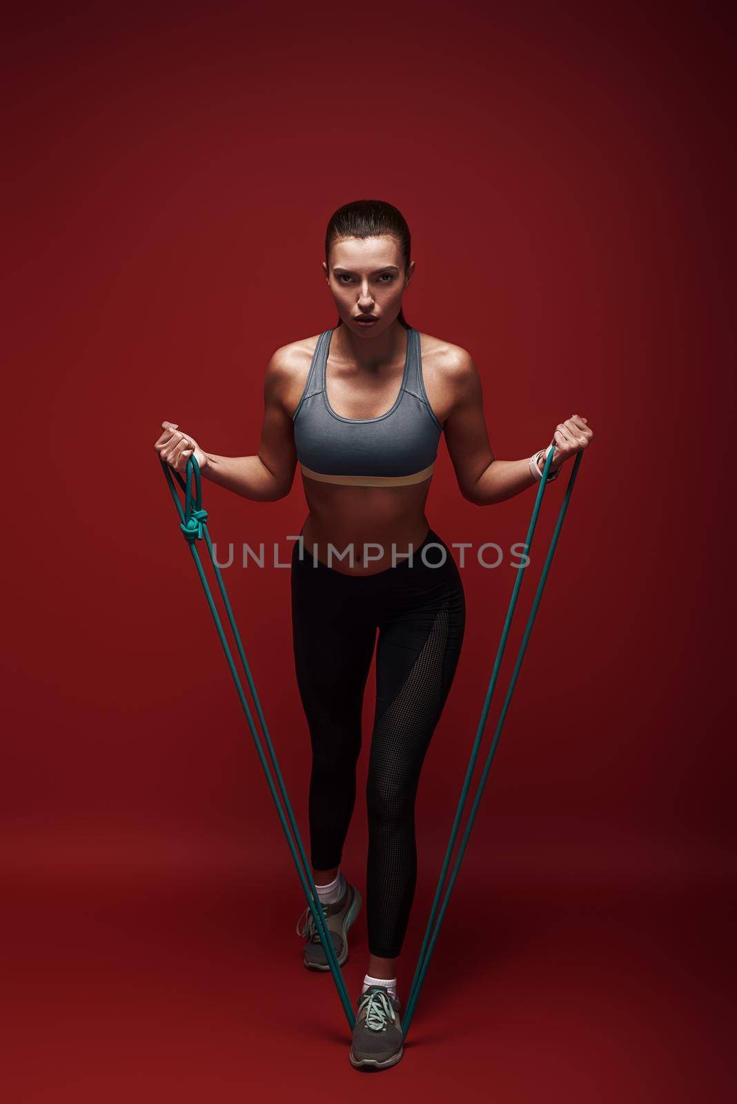 Belive in yourself. Beautiful sportswoman performs exercises with resistance band over red background by friendsstock