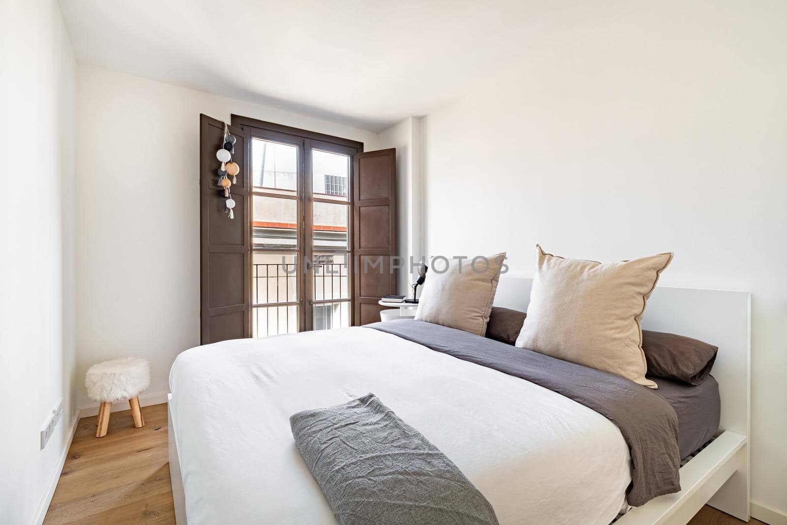 Bright bedroom with cozy bed, big pillows and window with city view. Interior of modern apartment in European city