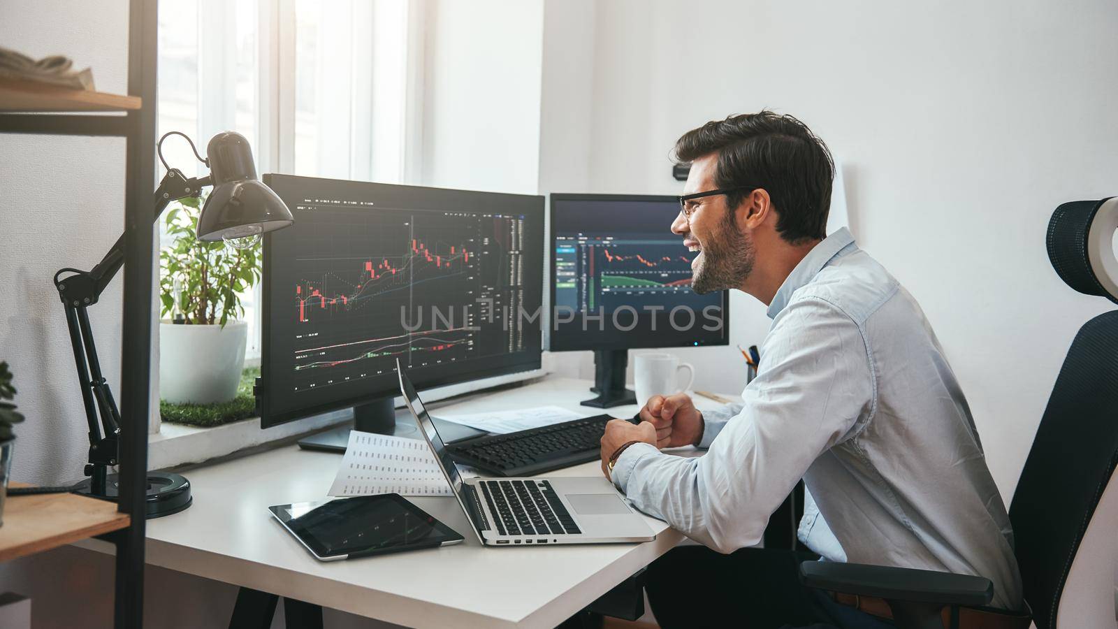 Great Happy young businessman or trader in formalwear looking at charts on computer screen in the office and smiling by friendsstock