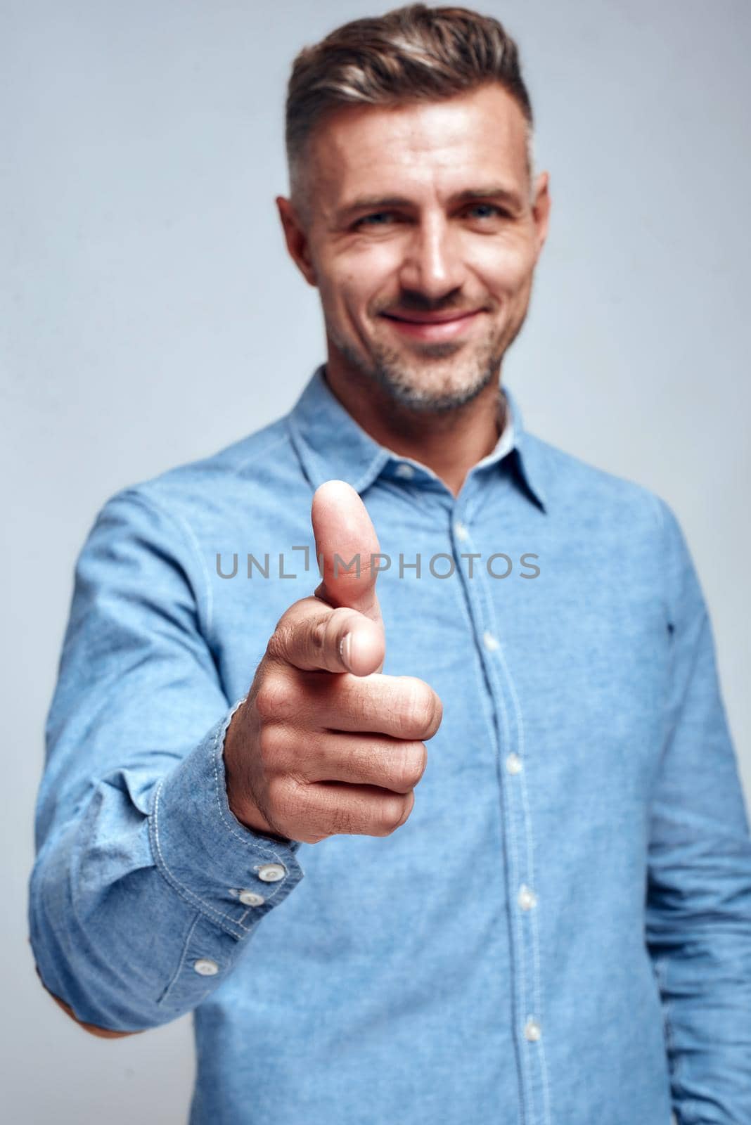 I am choosing you. Smiling handsome man in blue shirt pointing his finger and smiling at camera while standing against grey background by friendsstock