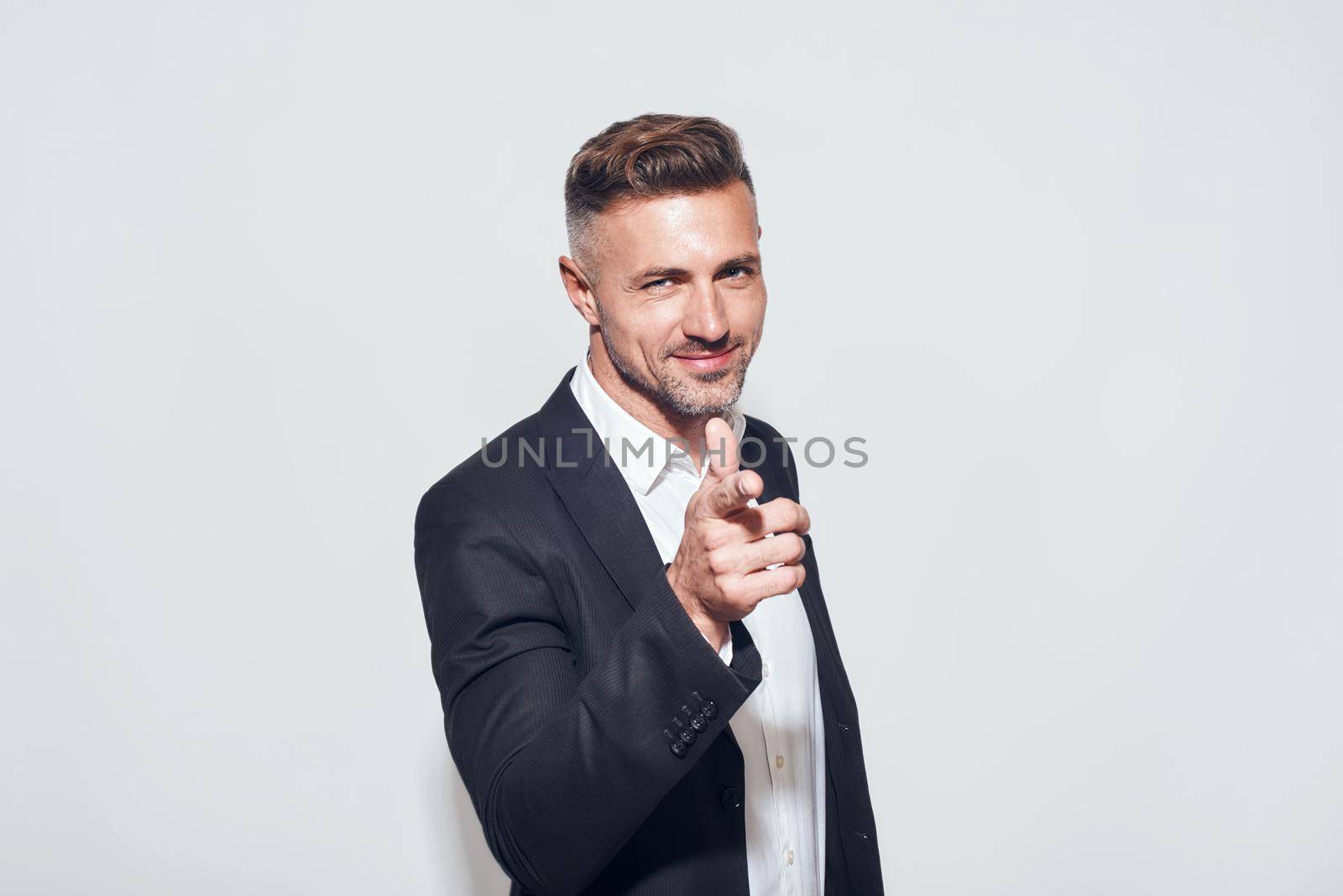 Studio shot of cheerful bearded businessman in classic suit gesturing and smiling while standing against grey background. Men beauty. Business look. Studio shot