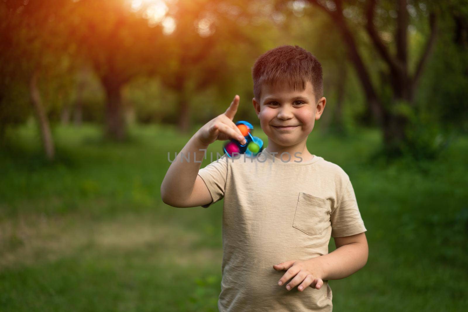 Funny Smiling Boy Playing with Spinner in a Sunny Day in the Park. 6 Years Old Guy Has a Spinner in his Hand. Outdoor with Son. High quality photo