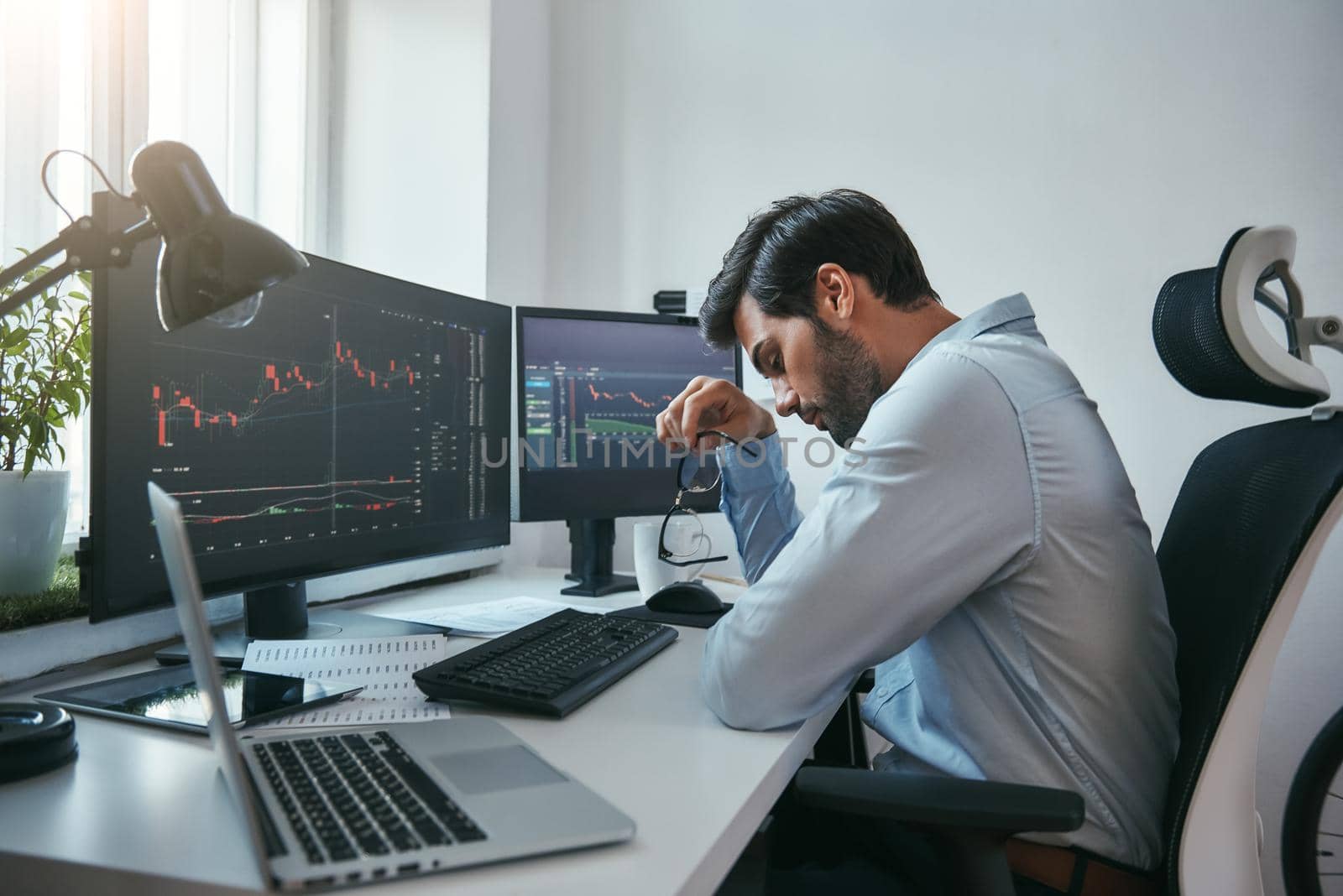Time to take a break. Side view of tired young businessman or trader holding eyeglasses and feeling tired while working with data and charts on computers at his modern office. Forex market. Trade concept. Business concept