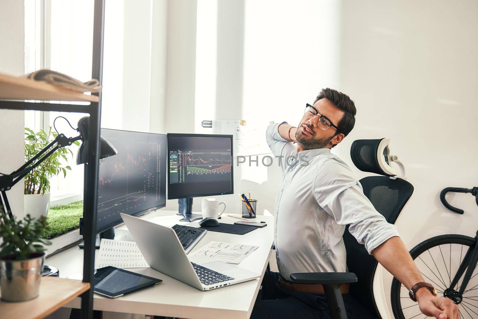 Feeling exhausted. Tired young beard businessman or trader in formal wear keeping eyes closed and stretching while sitting at his working place. Stock broker. Forex market. Trade concept
