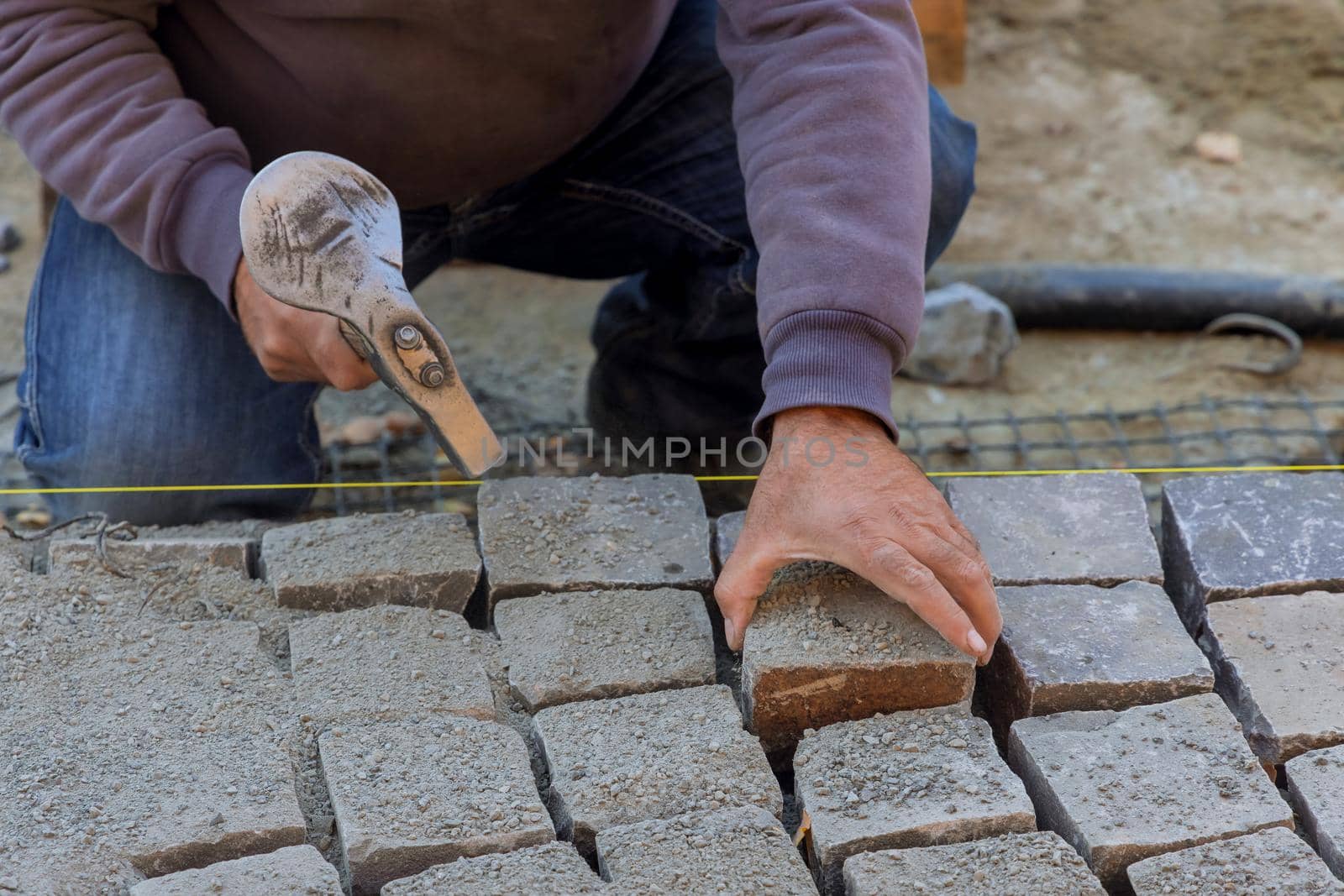 Road worker using stones and hammer to build stone road of construction laying stones by ungvar