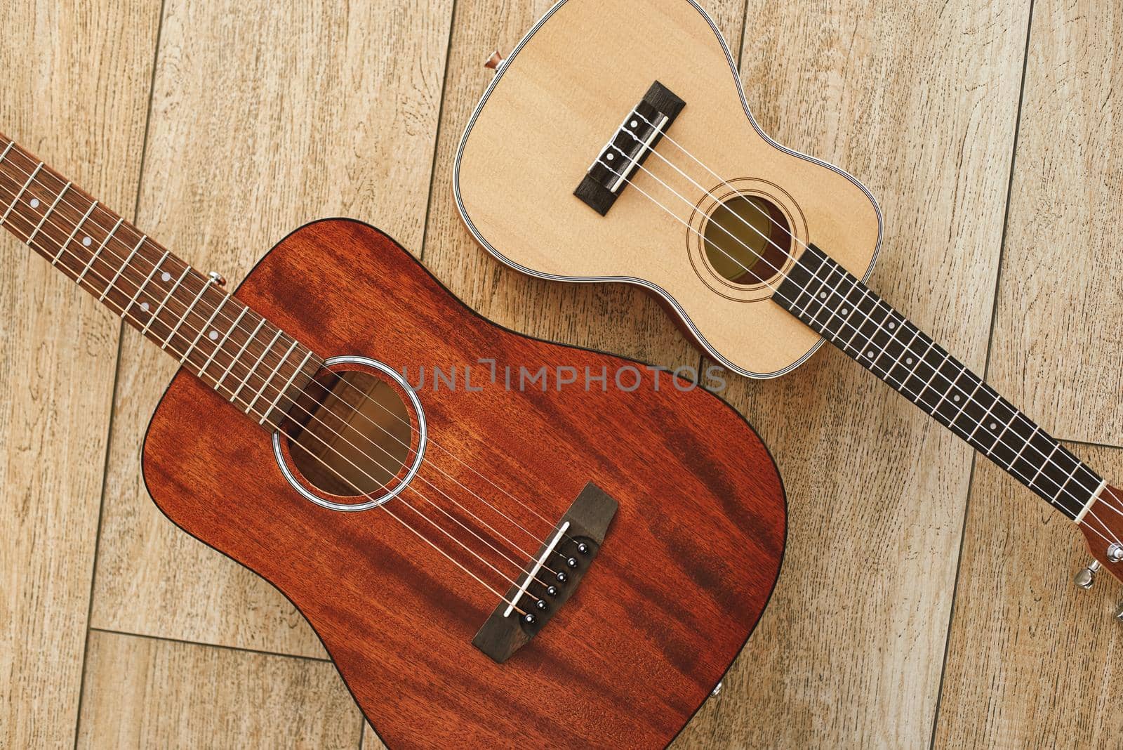 Perfect sound. Top view of the acoustic and ukulele guitars lying close to each other on the wooden floor. Music concept by friendsstock