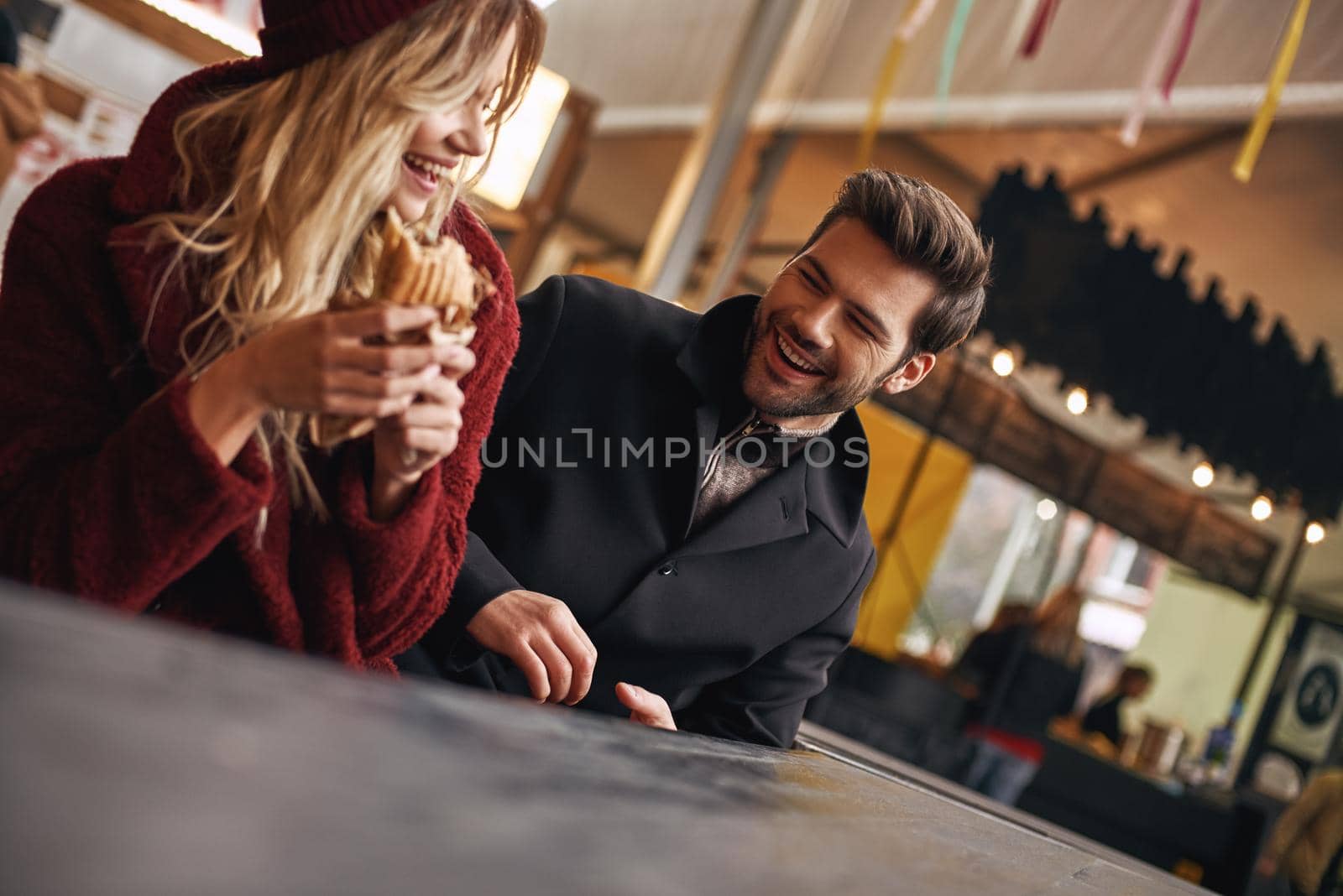 Close-up of young couple are eating sandwiches at the street food market. by friendsstock