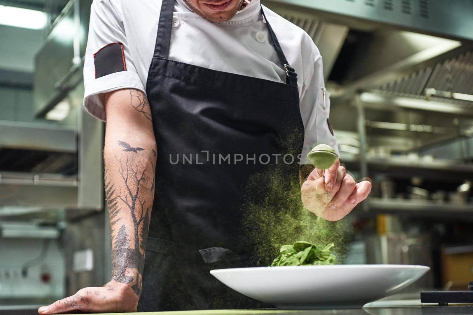 Slow motion. Cropped image of chef's hands with tattoos adding spices in salad while standing in a restaurant kitchen. by friendsstock