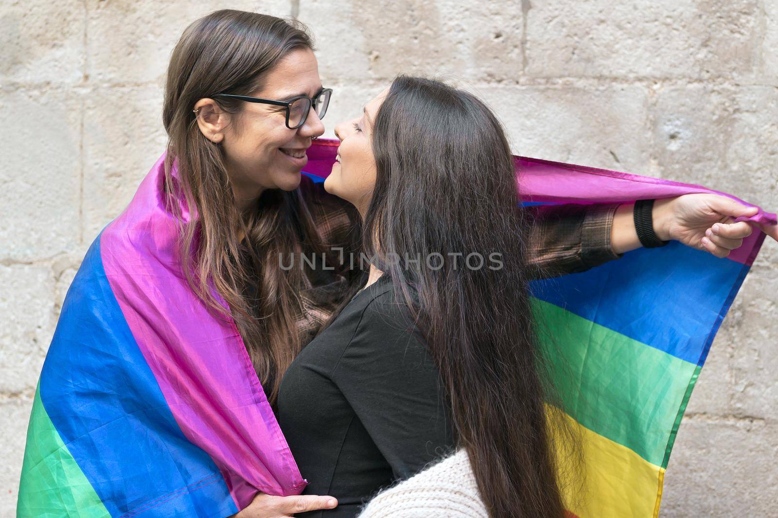 Portrait of an affectionate young lesbian couple hugging each other while standing together in front of a stone wall outside. High quality photo.