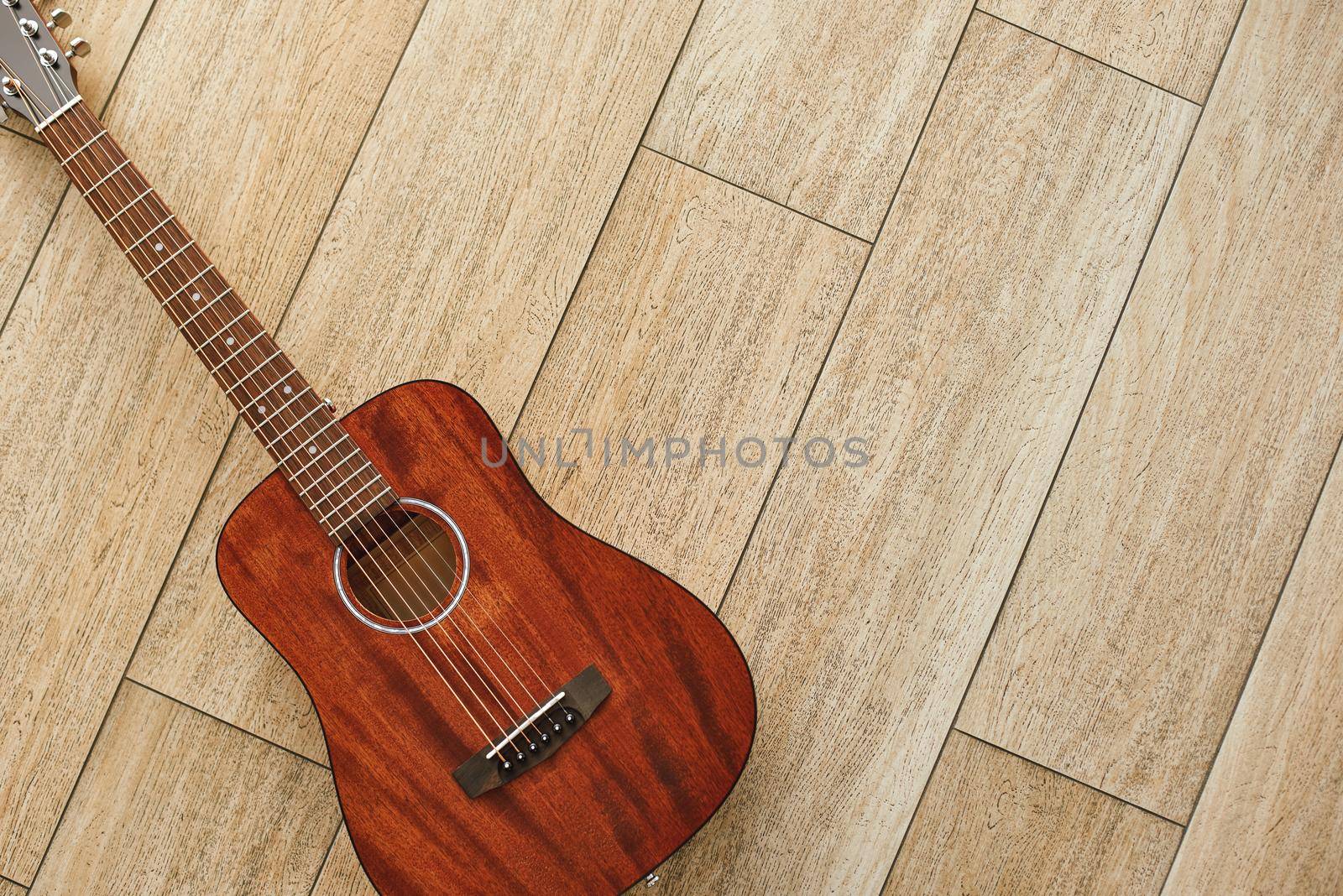 Beauty of musical instrument. Top view of the brown acoustic guitar lying on the wooden floor. by friendsstock