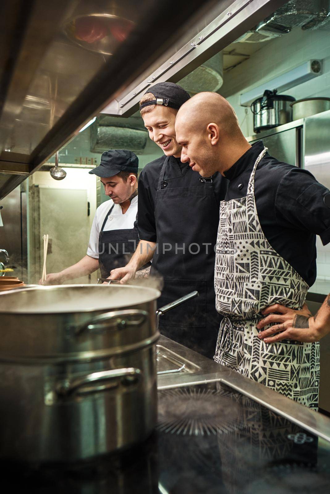 Great job. Cheerful professional chef looking how his two assistants are cooking in a restaurant kitchen. Preparing food