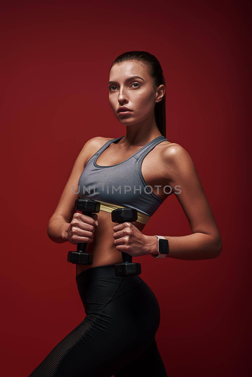 Love yourself enough to work harder. Sportswoman holds dumbbells standing over red background, looking away by friendsstock