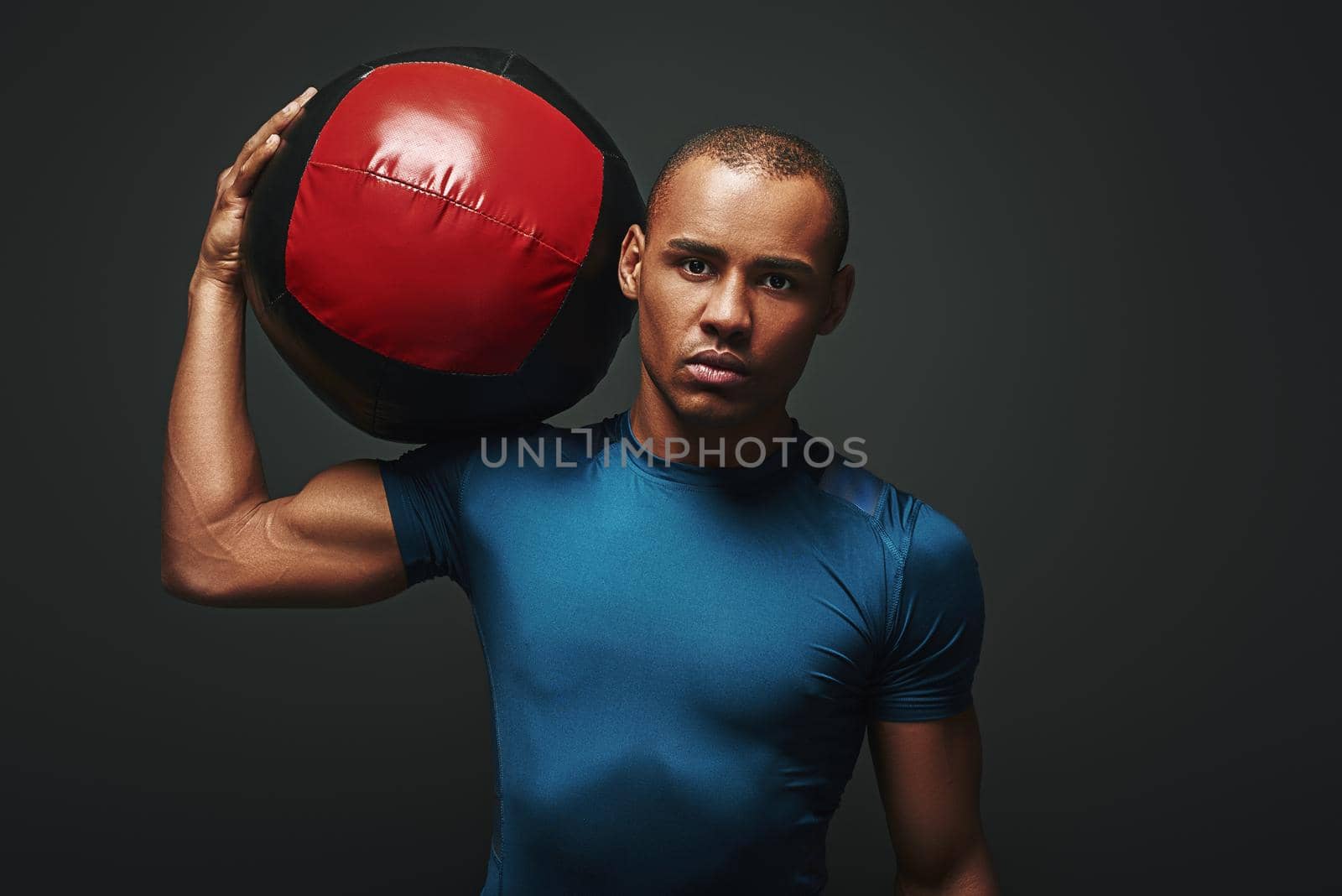 Close up portrait of a crossfit male athlete working out with exercise ball. Handsome muscular athletic sportsman standing with the ball over dark background in studio. Endurance concept