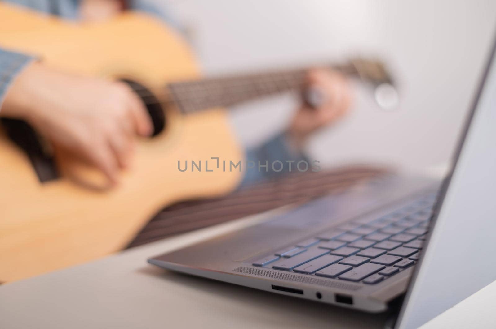Young caucasian woman with short blonde hair playing guitar and watching training video on laptop