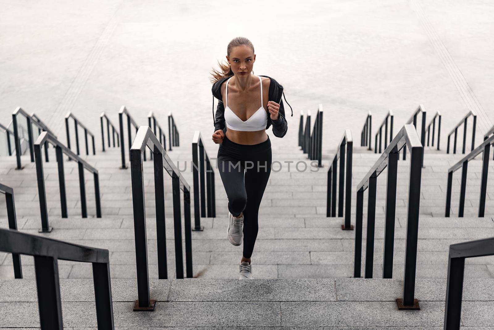 Sporty young woman is running upstairs outdoors. Front view by friendsstock