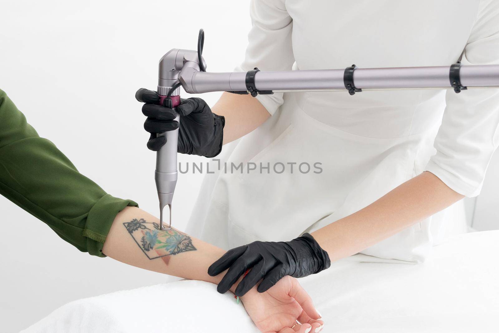 Beautician using laser device to remove an unwanted tattoo from female arm. Concept of erasing tattoos as expensive procedure in a cosmetology clinic