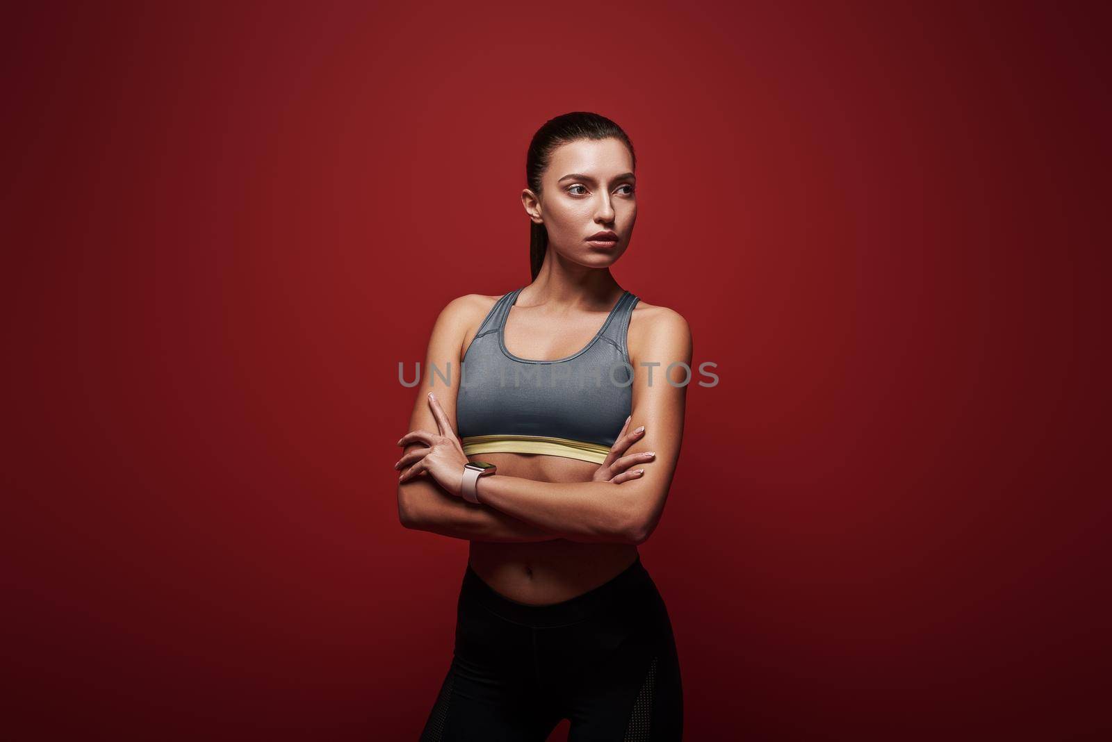 Portrait of a beautiful fit young sportswoman standing over red background, with crossed arms.