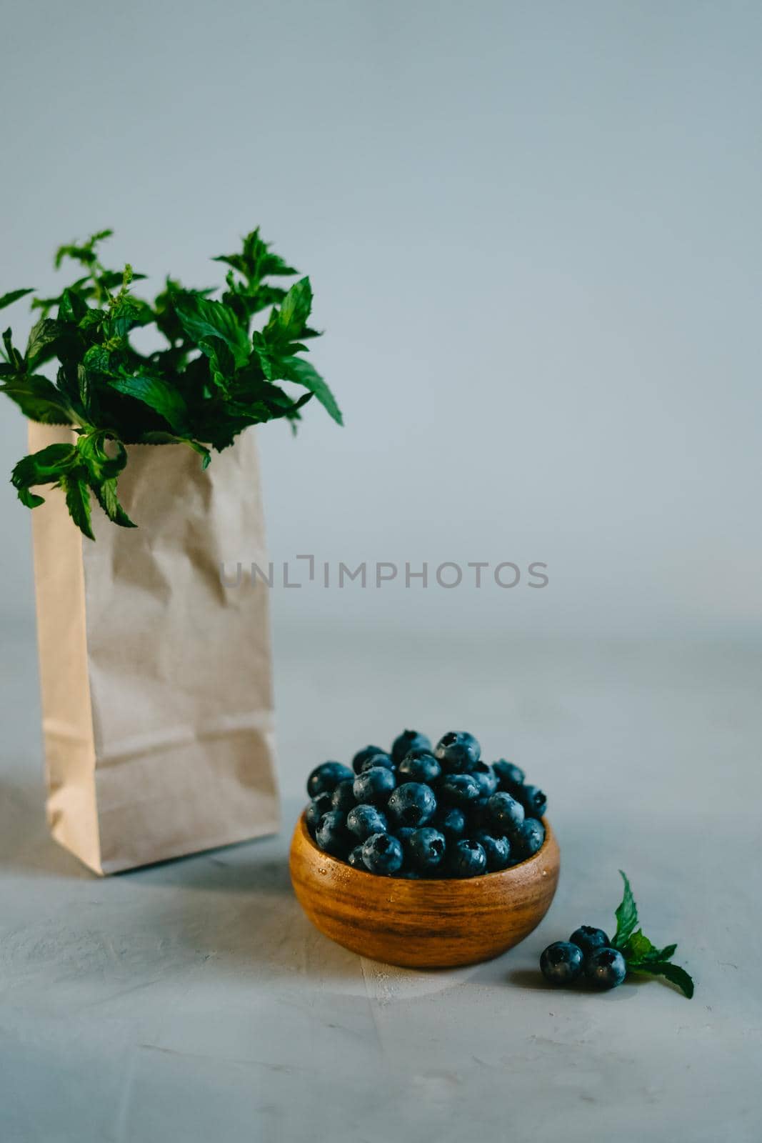 A small wooden bowl with berries. Juicy and ripe blueberries in an eco-friendly dish. Sprigs of fresh mint in a kraft bag. The concept of healthy eating and nutrition