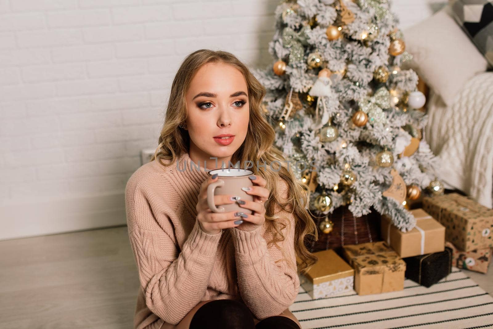 Happy young lady with long hair near fireplace and the Christmas tree, gifts. New year concept.