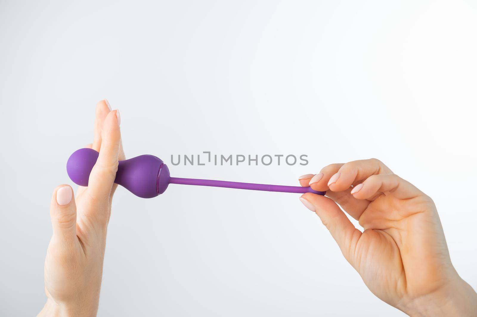 A faceless woman holding an electronic Kegel trainer for training pelvic floor muscles on a white background. Sex toy synchronized with a smartphone by mrwed54
