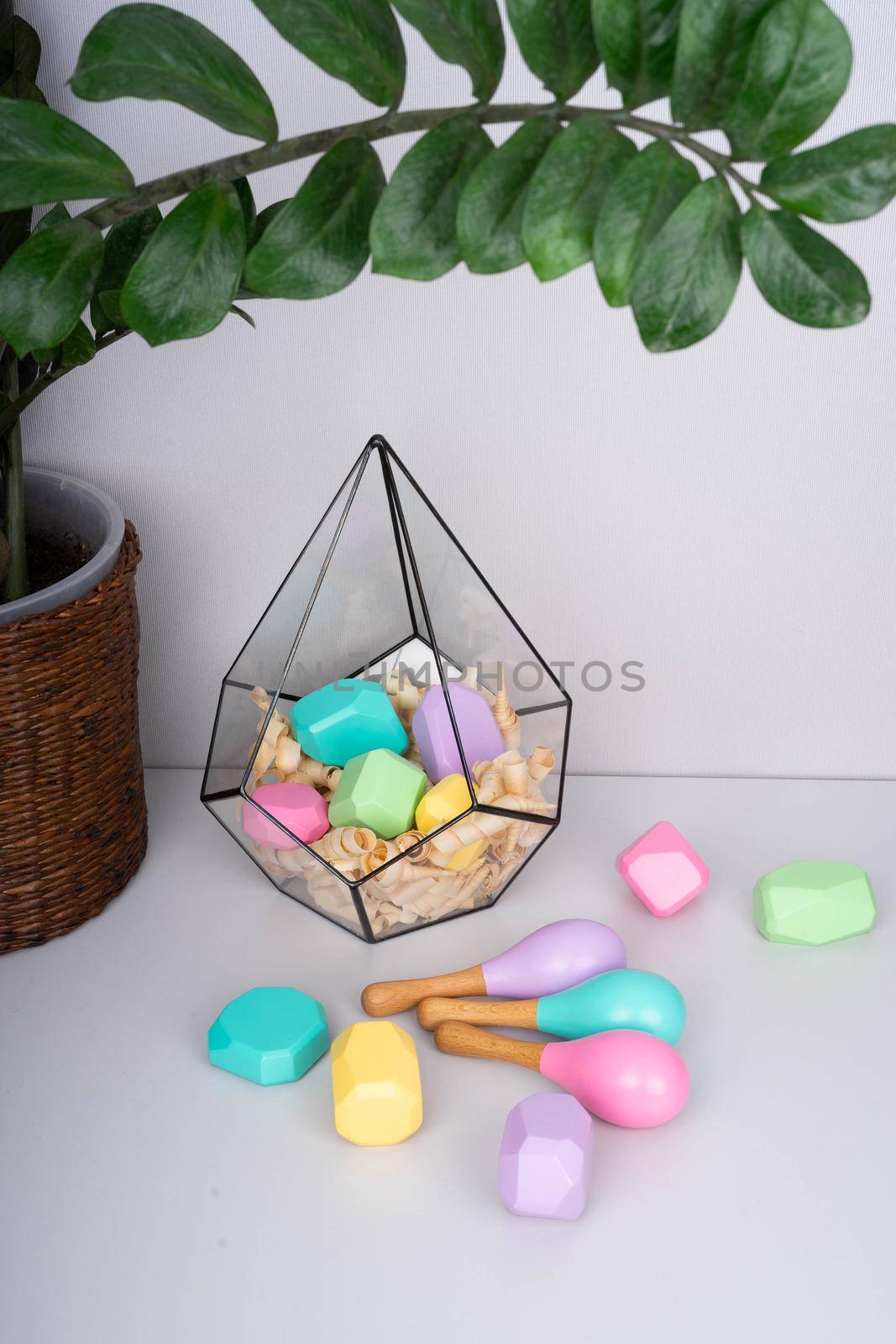 Children's wooden constructors in a glass florarium. Colored cubes of various shapes. Baby maracas. Green branch of houseplants.