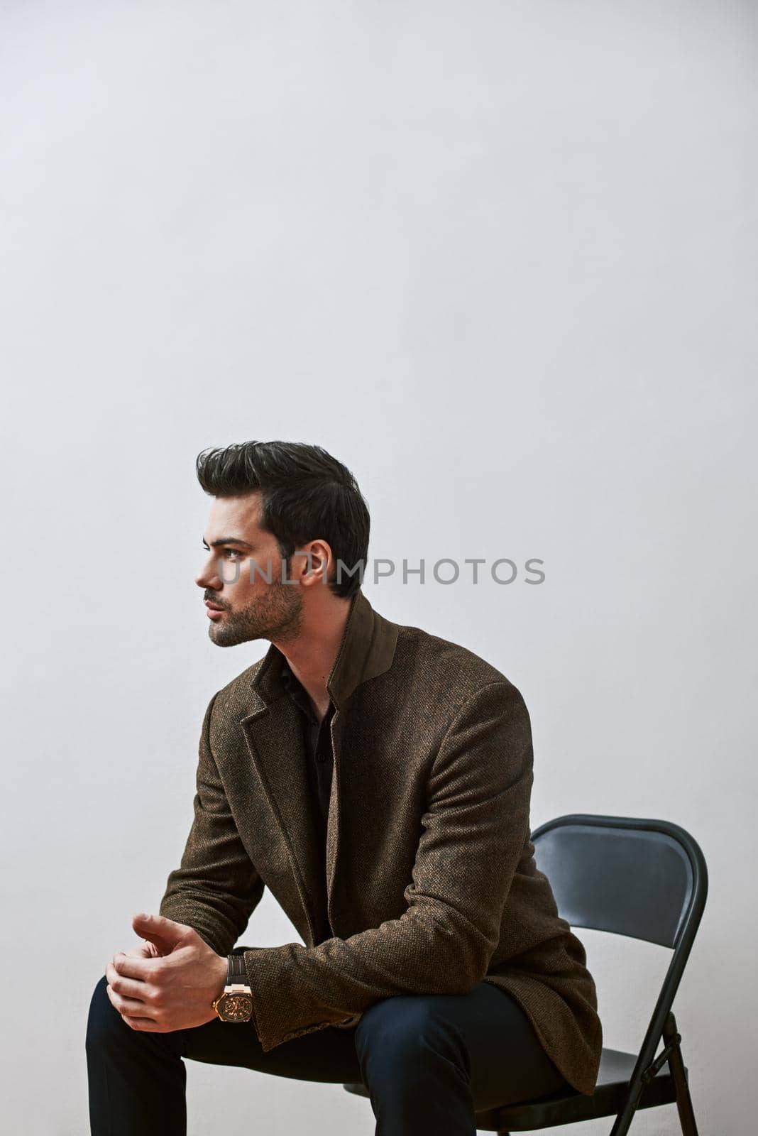 Confident and handsome. Fashionable young man sitting on a chair with his hands on his knees, looking away isolated over white background by friendsstock