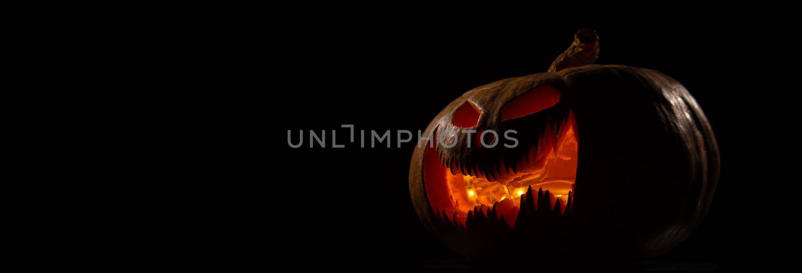 A creepy pumpkin with a carved grimace glows. Jack on a lantern in the dark