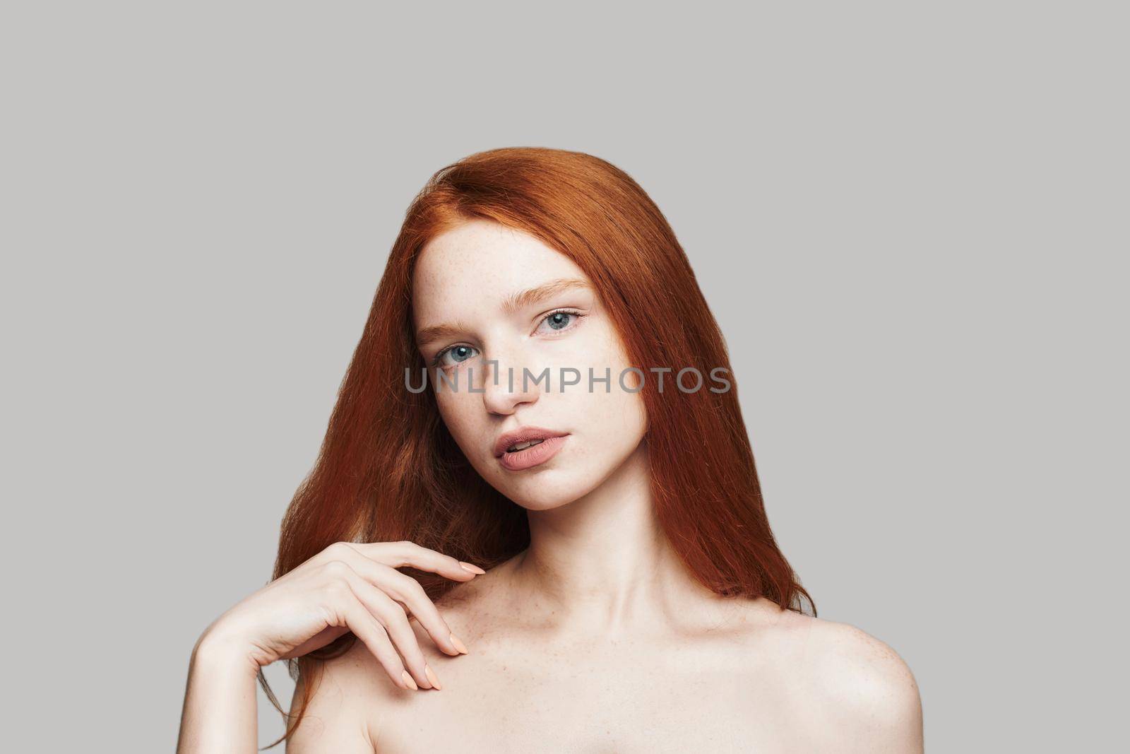 Studio shot beautiful woman with long red hair looking at camera while standing against grey background. Beauty portrait