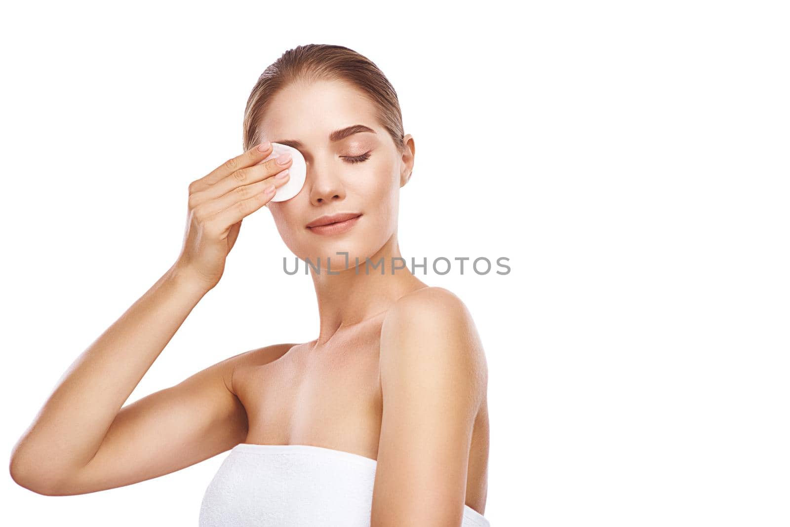 Beautiful woman cleans her face with sponge, she wearing white towel, close-up studio photo on white background. Light hair, grey eyes