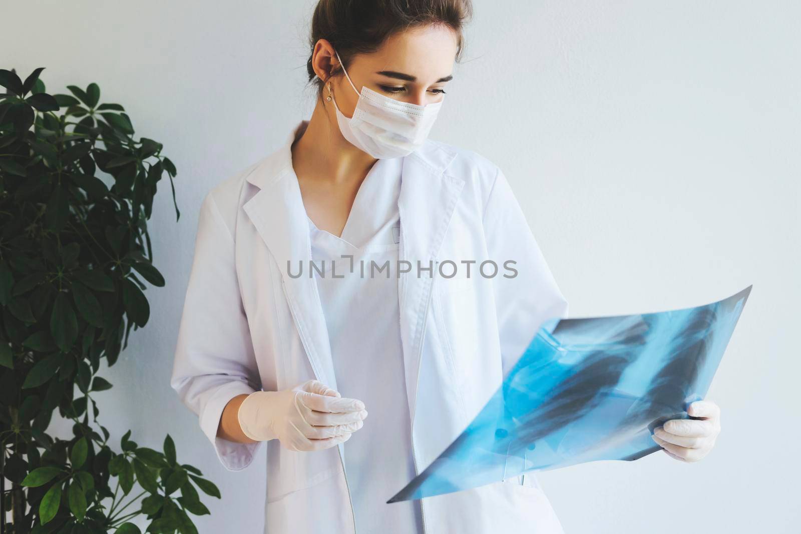 A radiologist in a medical mask and gloves radiates an x-ray image of the patient's lungs. The girl doctor works on the front line. The doctor is holding an X-ray of his lungs.