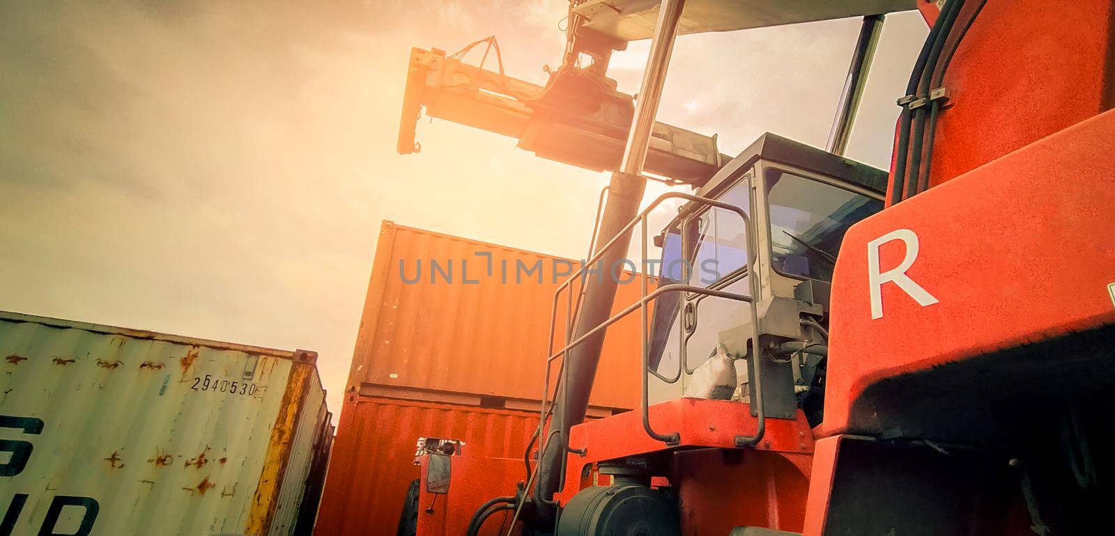 Reach stacker lifting container. Forklift truck handling container at dock. Reach stacker vehicle. Container transport in logistic industry. Cargo and shipping business. Import and export logistic. by Fahroni