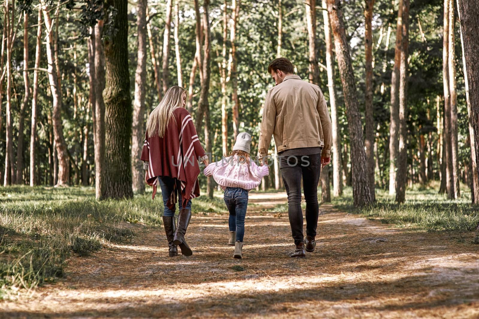 Young parents with little daughter in autumn forest. Mom and dad holding baby girl. Rear view