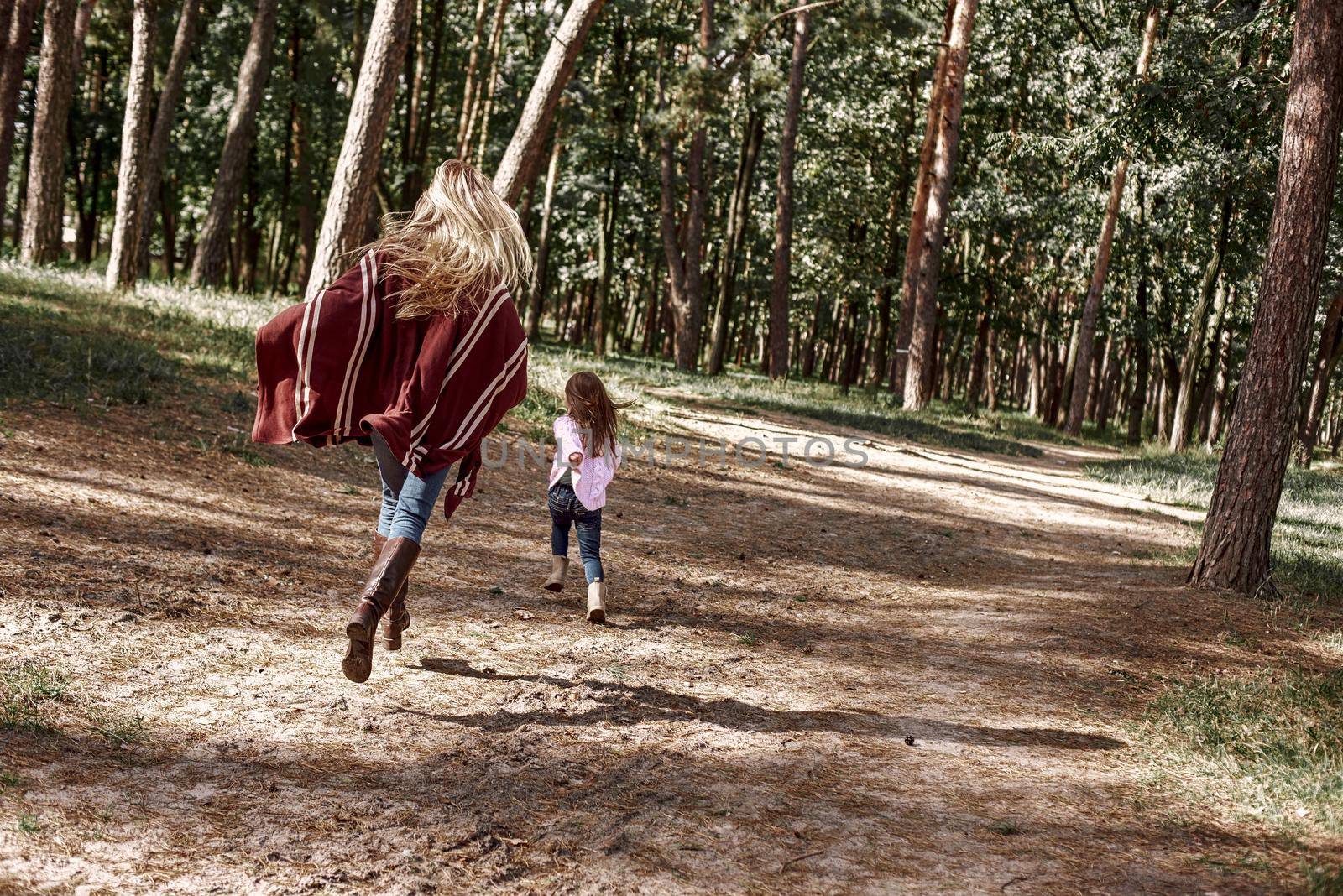 Happy, stylish little curly girl is running with her beautiful mother in forest. by friendsstock