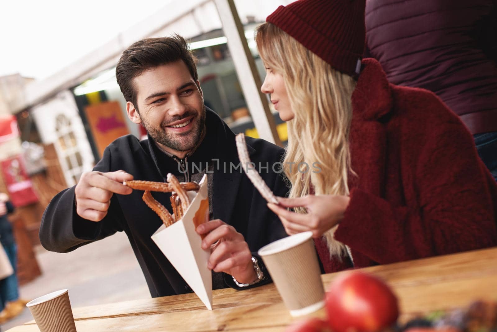 Couple are eating outdoors . Young couple are eating churros at the street food market. Cold season. Close-up photo of couple eating from one package