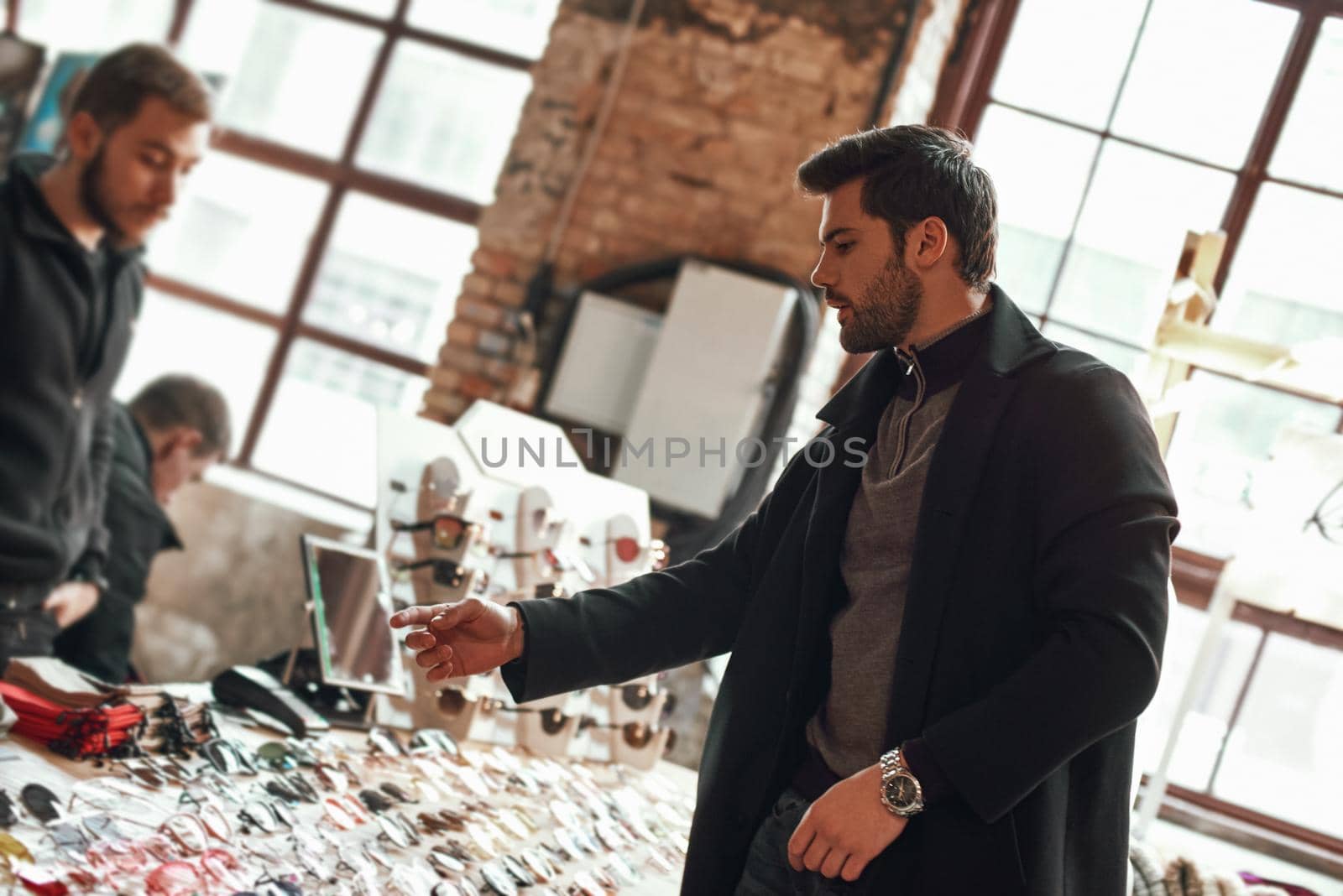 Young stylish man in coat choosing glasses. Customer in street market choosing the eyeglasses from a shelf with many different models