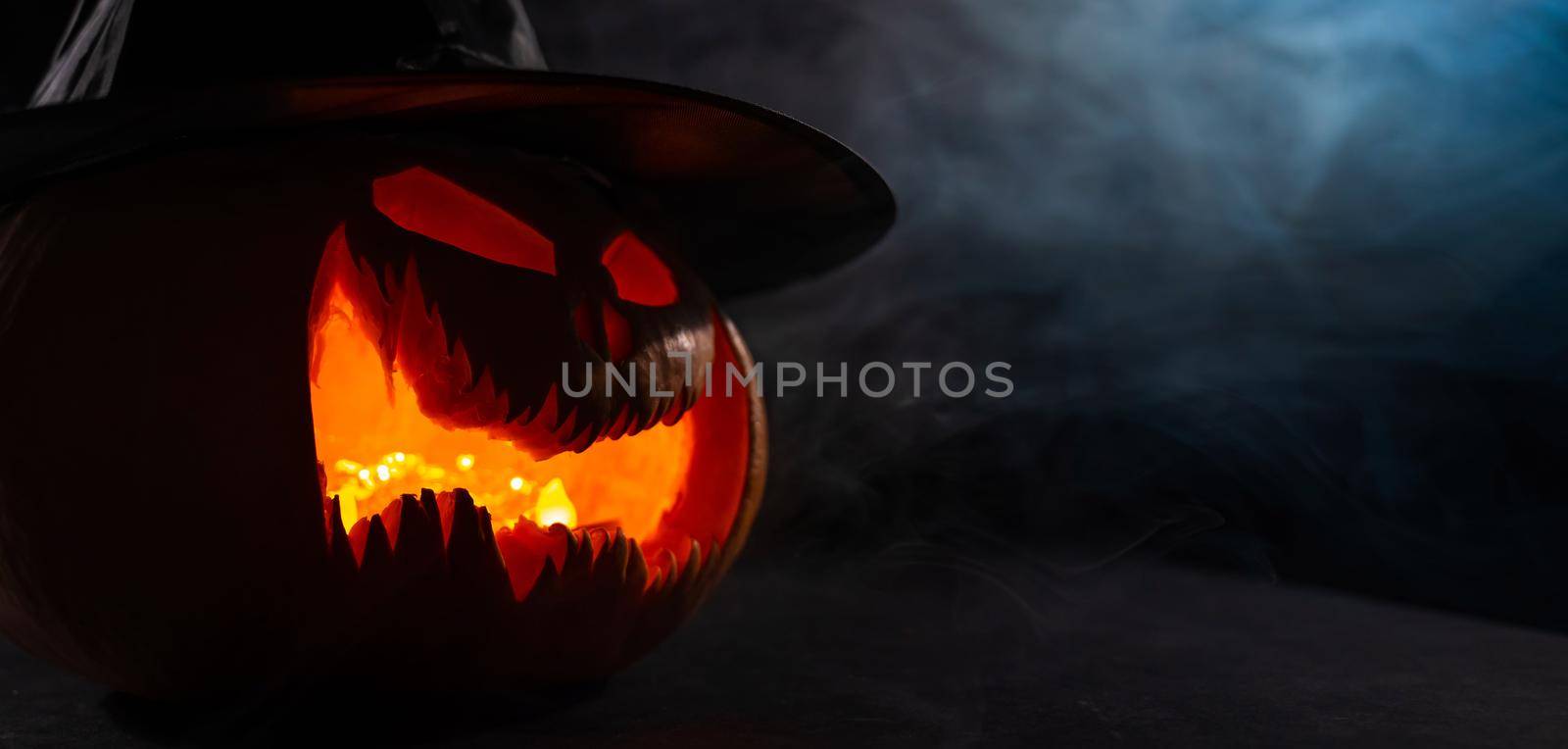 A creepy pumpkin with a carved grimace in the smoke. Jack o lantern in the dark