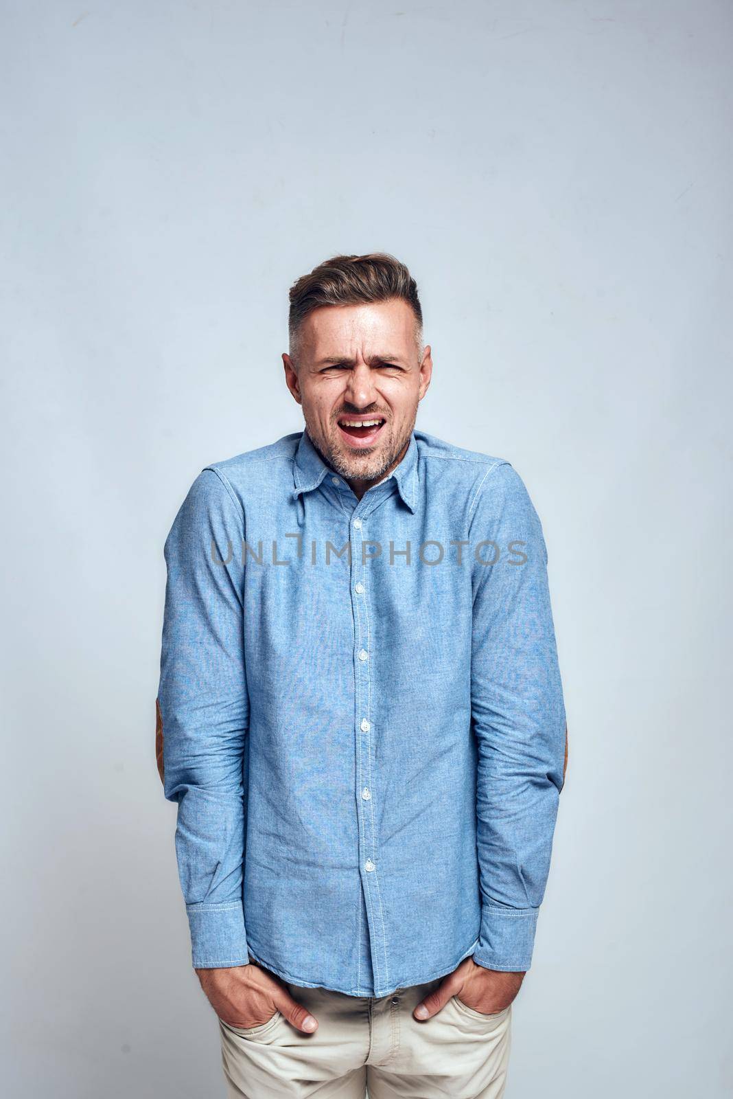 I don't like it. Frustrated young man keeping hands in his pockets and making unhappy face while standing against grey background by friendsstock