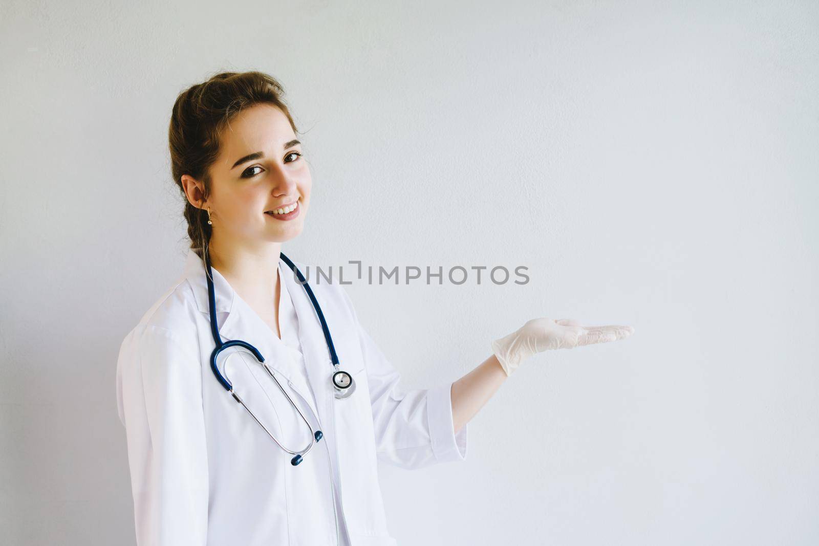 A beautiful doctor girl. A medic on a pure white background. The doctor points to an empty space for text. Doctor with a smile on her face points her hand in a rubber glove to an empty place.