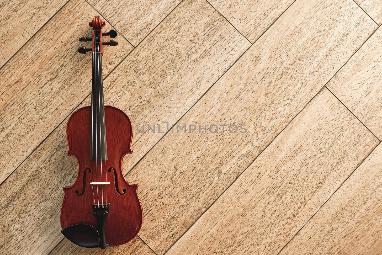 Classic musical instrument. Top view of the brown violin lying on the light wooden floor. Musical instruments. Music equipment. Music background