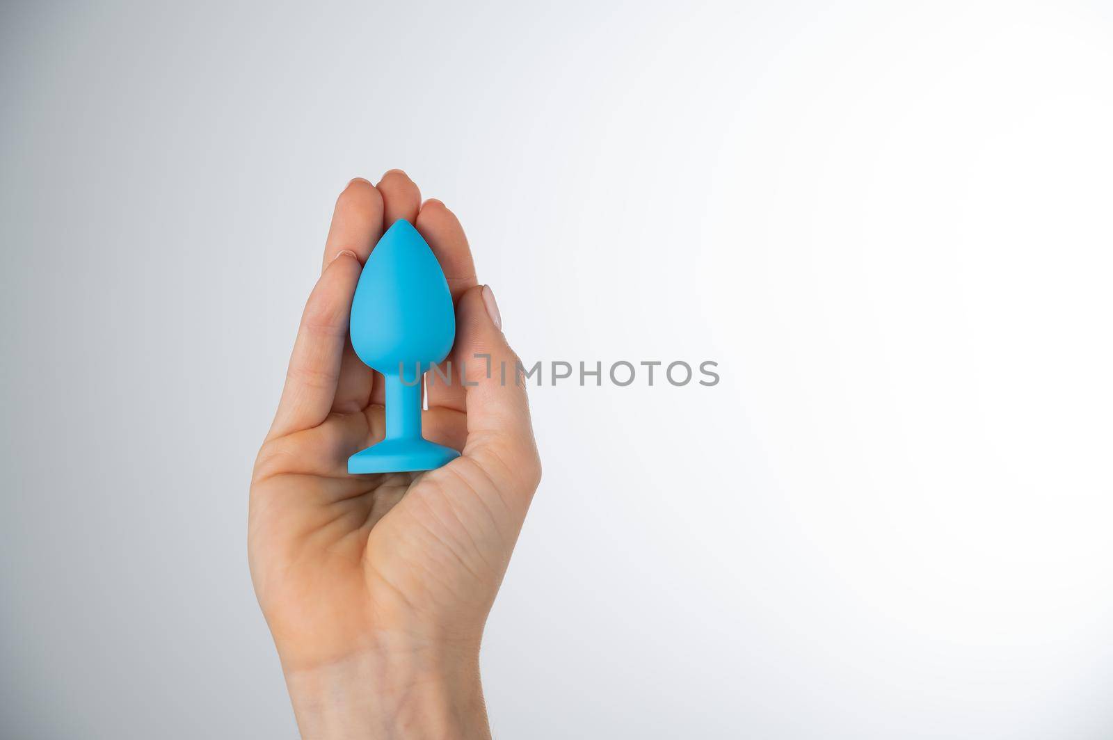 Woman holding a blue anal plug on a white background. Adult toy for alternative sex.
