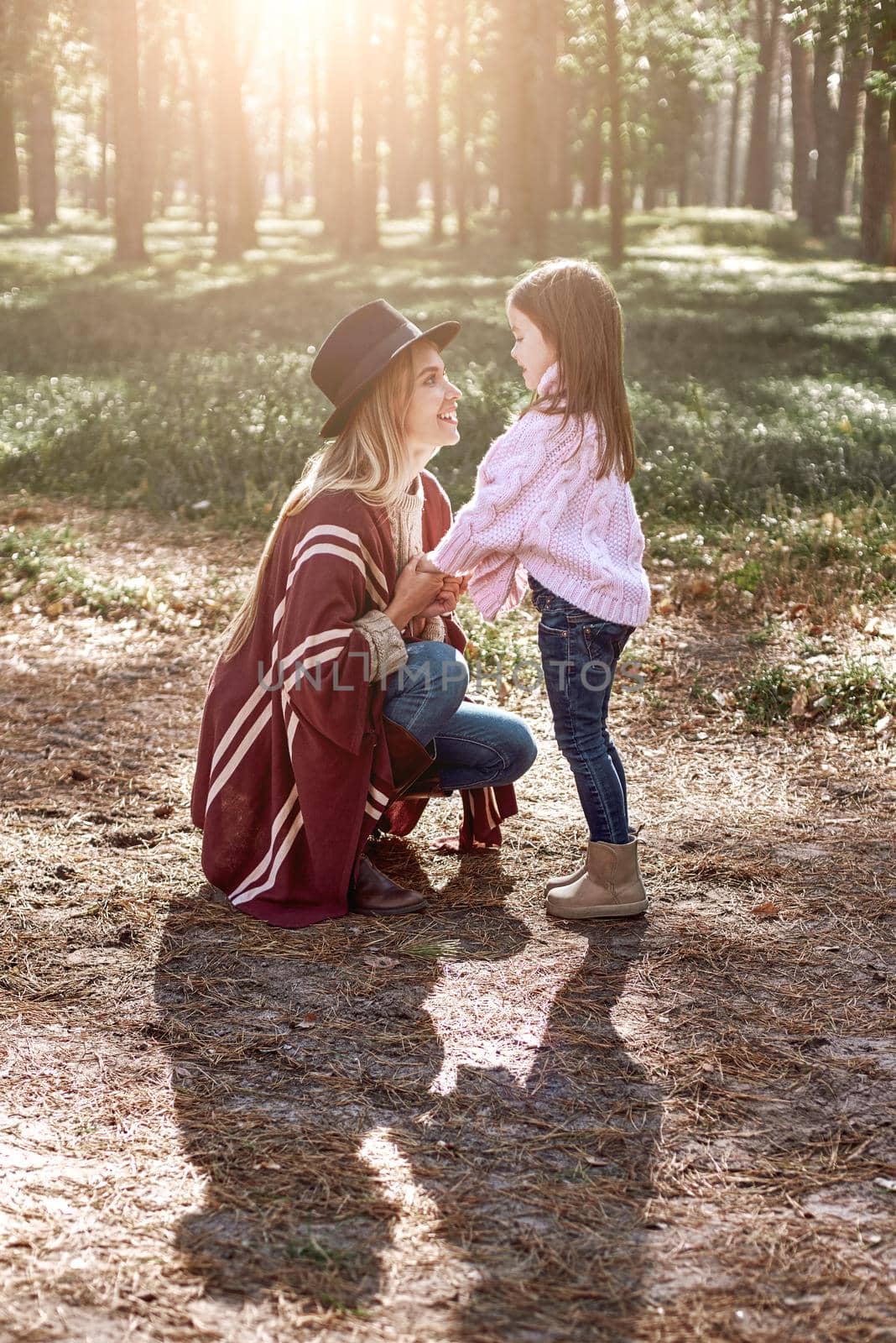 Little girl and her mother in the autumn park. Woman is wearing a stylish hat and knitted coat, girl is in pink bright sweater