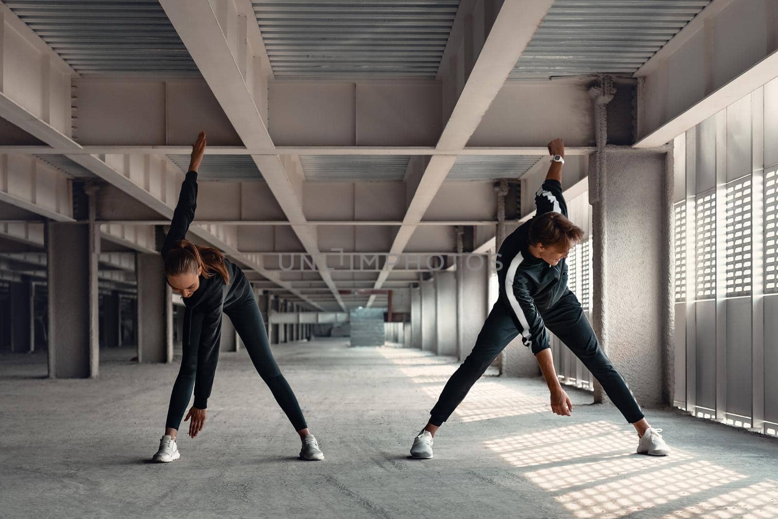 Young man and woman are doing warming up exercises at parking by friendsstock