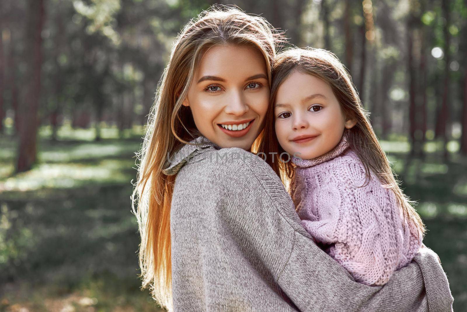 Happy, stylish little curly girl is hugging her beautiful mother in forest by friendsstock