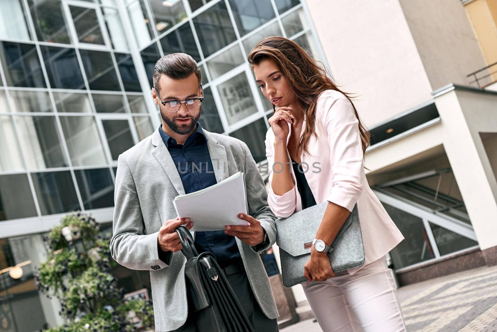 Preparation for meeting. Two young business people standing outside on the city street reading documents pensive